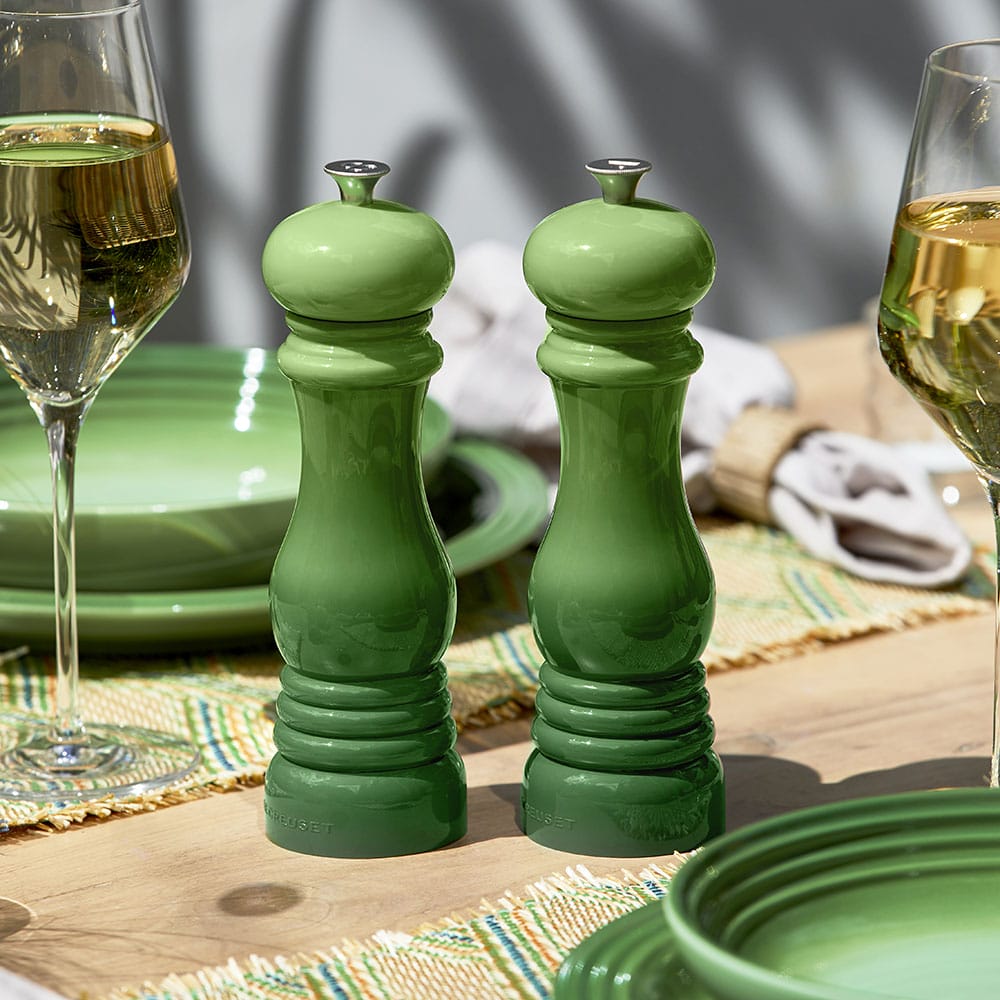 Two green salt and pepper shakers on a table with wine glasses and plates.