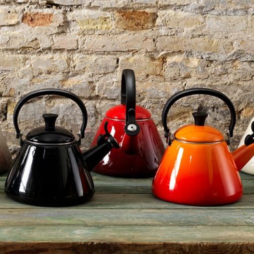 Set of colorful kettles on a wooden surface with a stone wall background