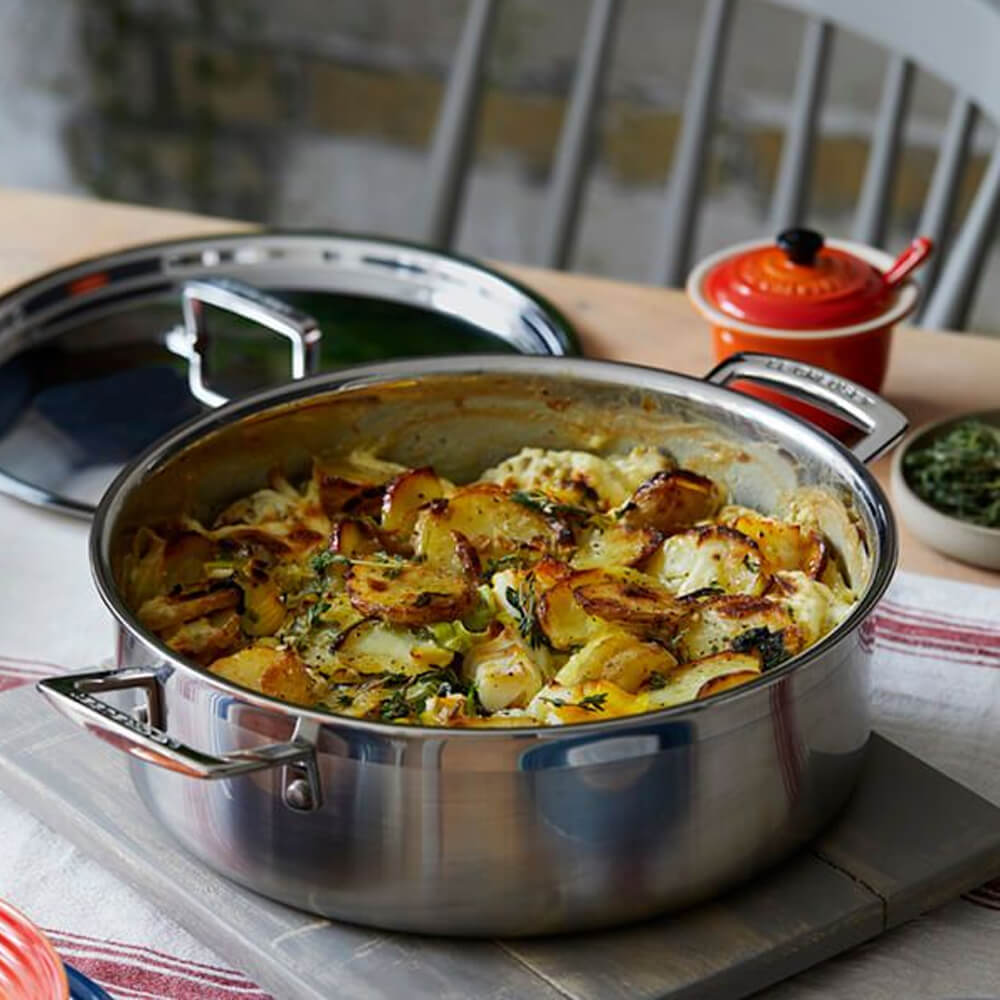 Stainless steel sauteuse with roasted vegetable dish on a kitchen counter