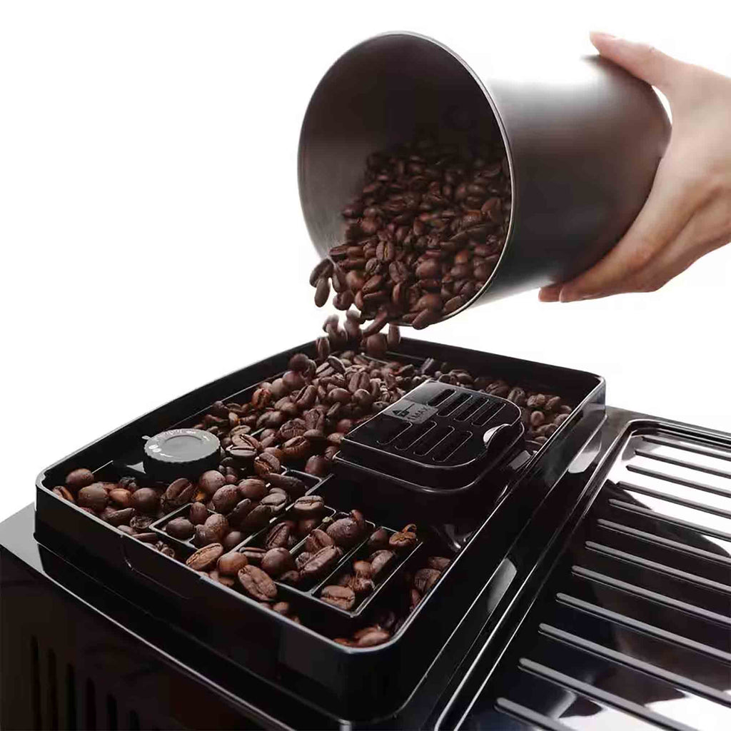 Hand pouring coffee beans into a coffee grinder filled with beans.