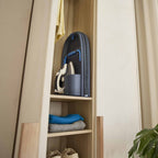 Wooden shelf with folded clothes and a foldable ironing board a neutral wall.