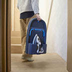 Person holding a blue foldable ironing board with an iron inside, standing in a room with wooden floor and white walls.