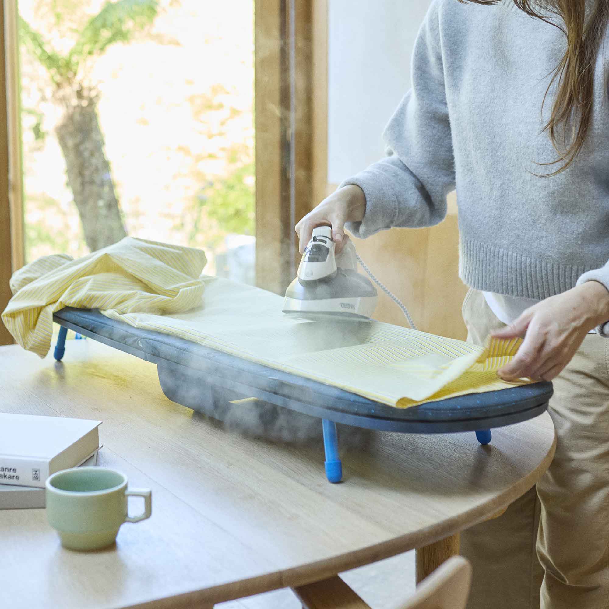 Person ironing a garment on a small table with a steaming iron