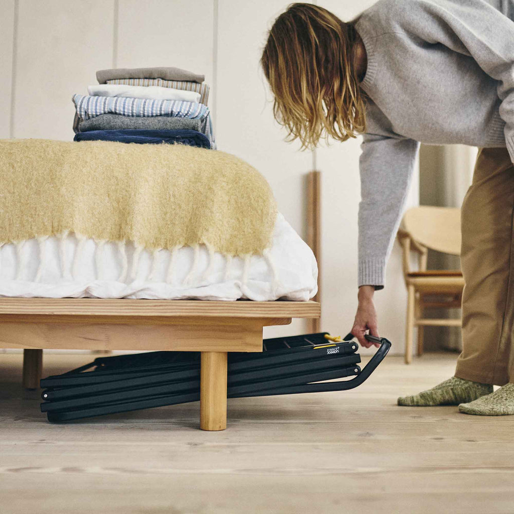 Person putting a clothes drier under a bed to store it