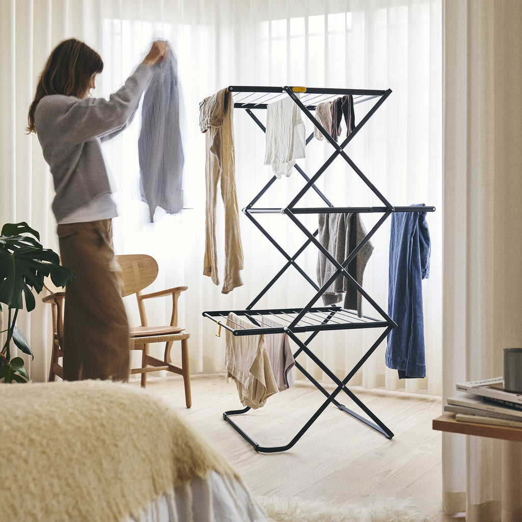 Person hanging clothes on a black drying rack in a bedroom.