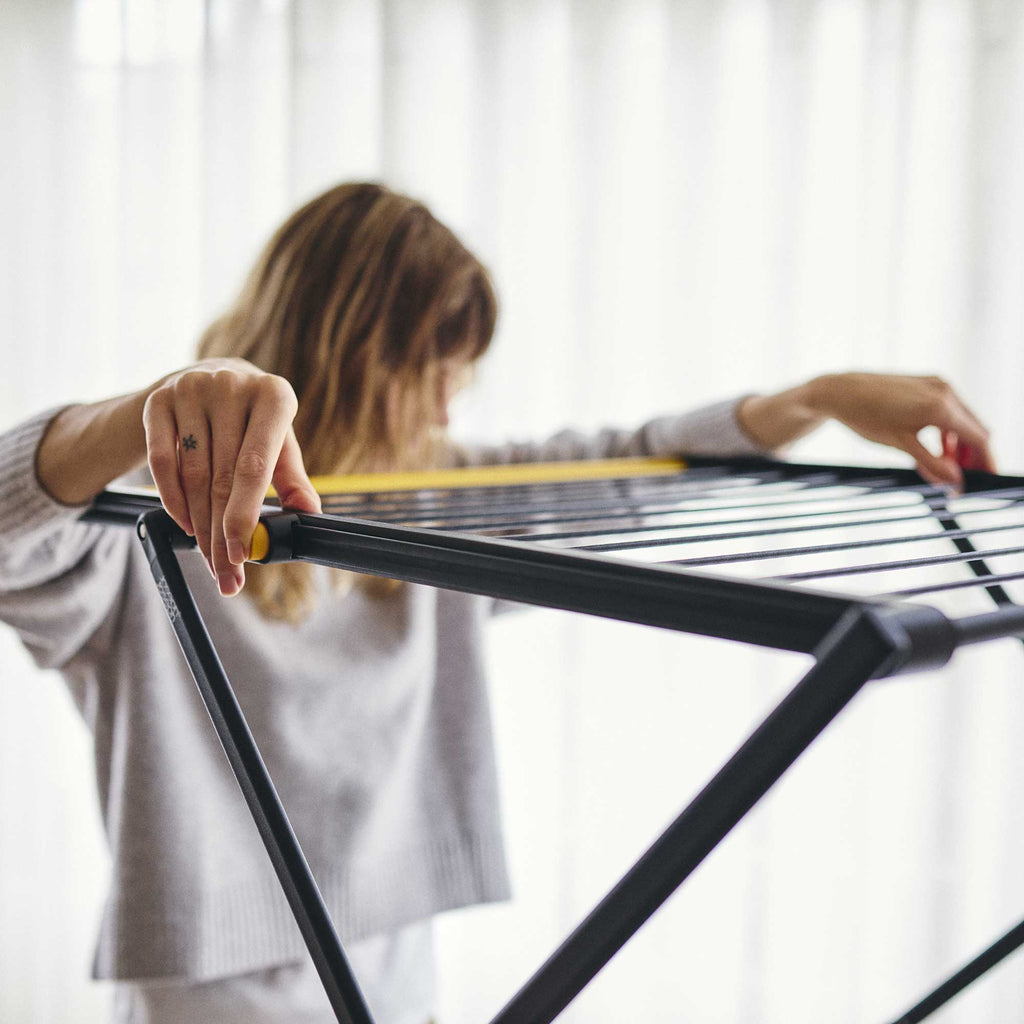 Person assembling a black metal clothes drier indoors.