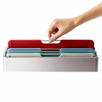 Hand removing a red chopping board from a chopping board set on a white background