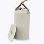 Beige laundry basket with a lid, filled with clothes, on a white background