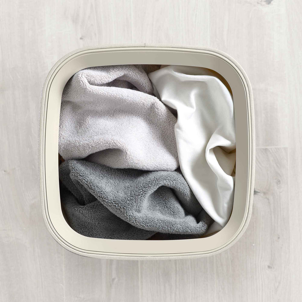 Folded clothes inside a white laundry basket on a light wooden floor.