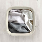Folded clothes inside a white laundry basket on a light wooden floor.