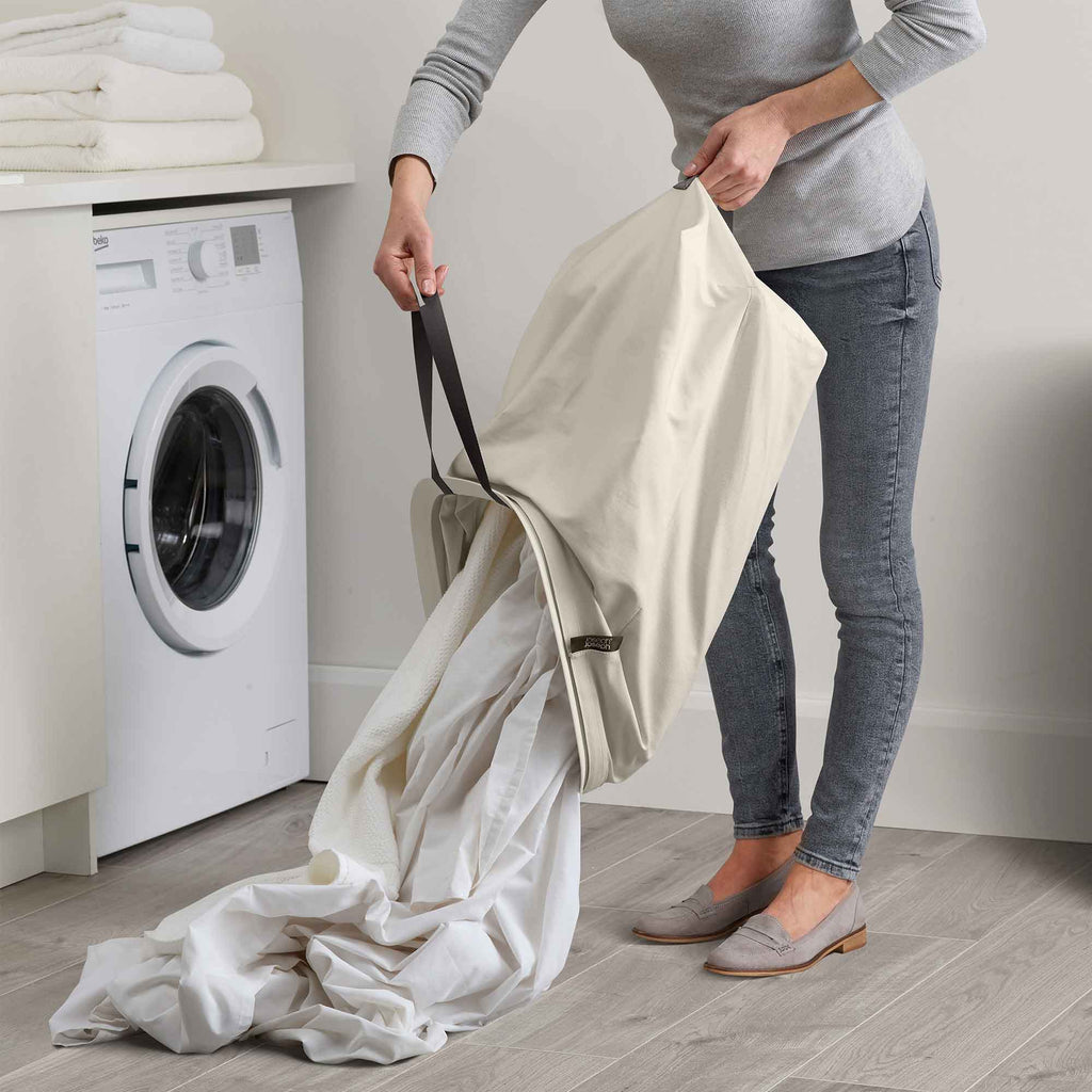 Person holding a large white garment bag in a laundry room with a washing machine.