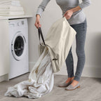 Person holding a large white garment bag in a laundry room with a washing machine.