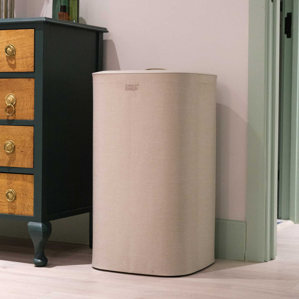 Beige cylindrical laundry basket next to a wooden dresser with black finish.