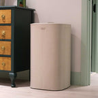 Beige cylindrical laundry basket next to a wooden dresser with black finish.