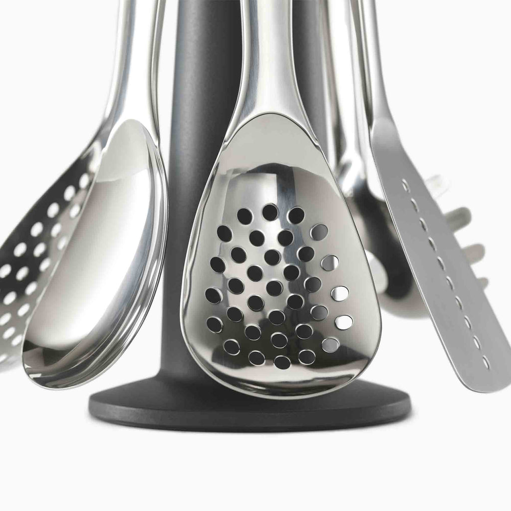 Set of stainless steel kitchen utensils on a black stand against a white background