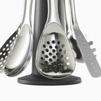 Set of stainless steel kitchen utensils on a black stand against a white background
