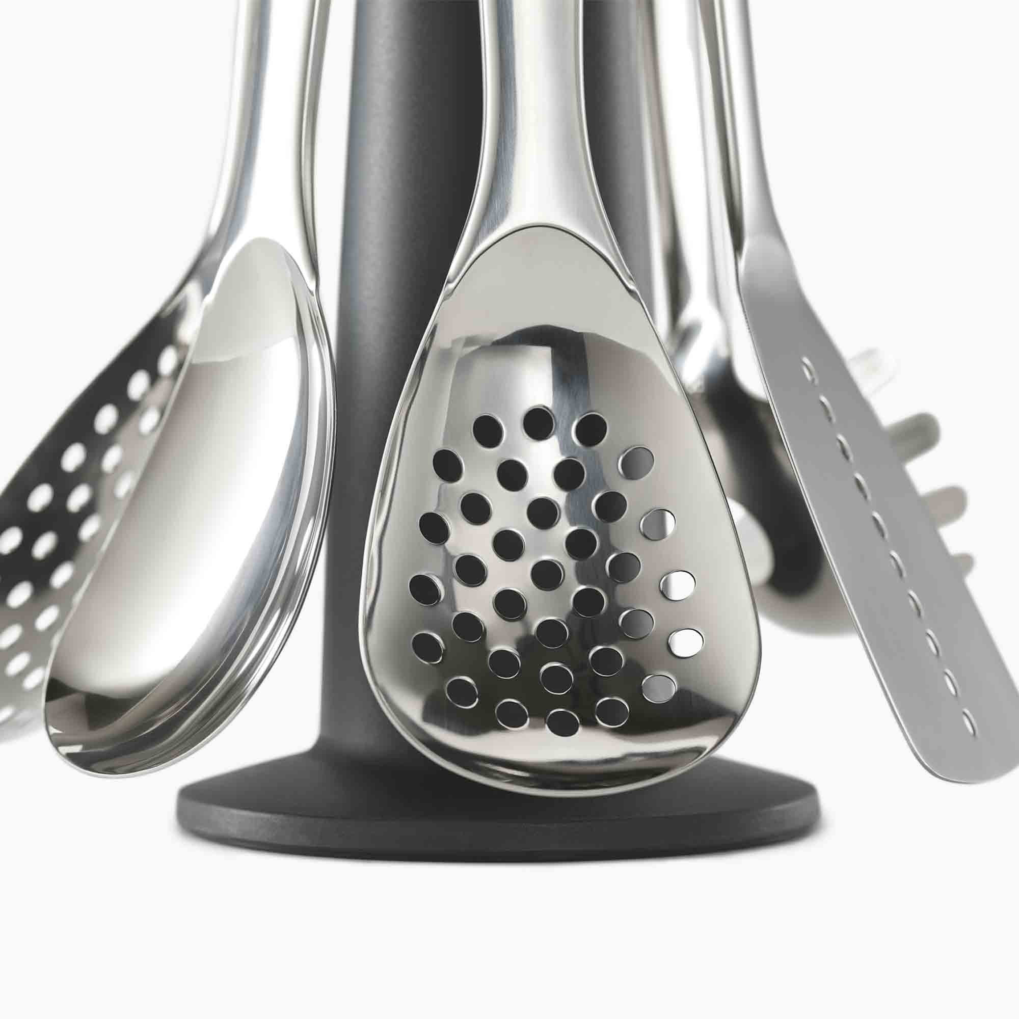 Set of stainless steel kitchen utensils on a black stand against a white background
