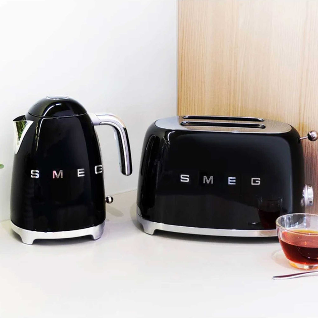 Black Smeg kettle and toaster on a white surface with a wooden wall in the background.