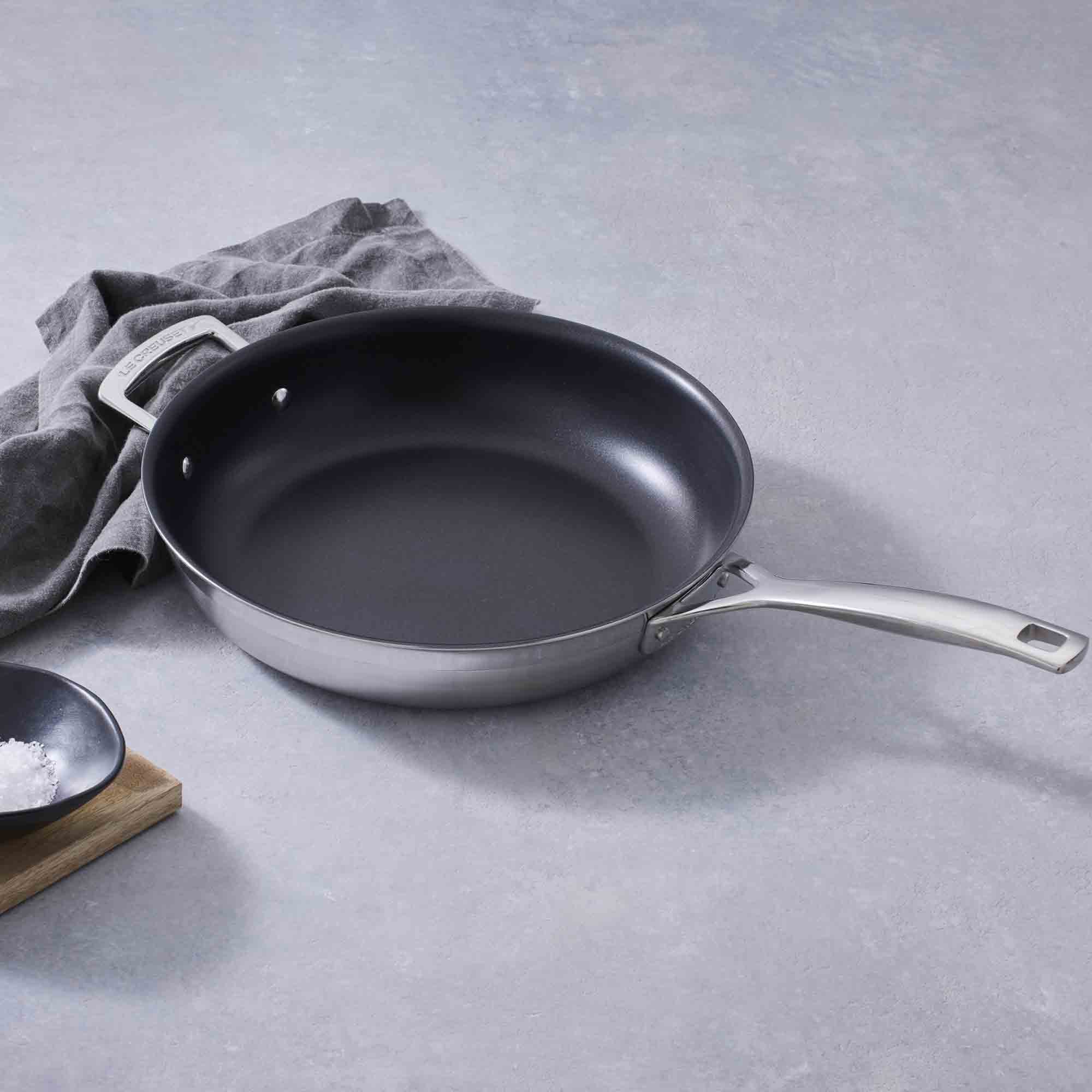 Le Creuset 3-ply Stainless Steel Non-Stick Frying Pan with Helper Handle on grey background with grey cloth