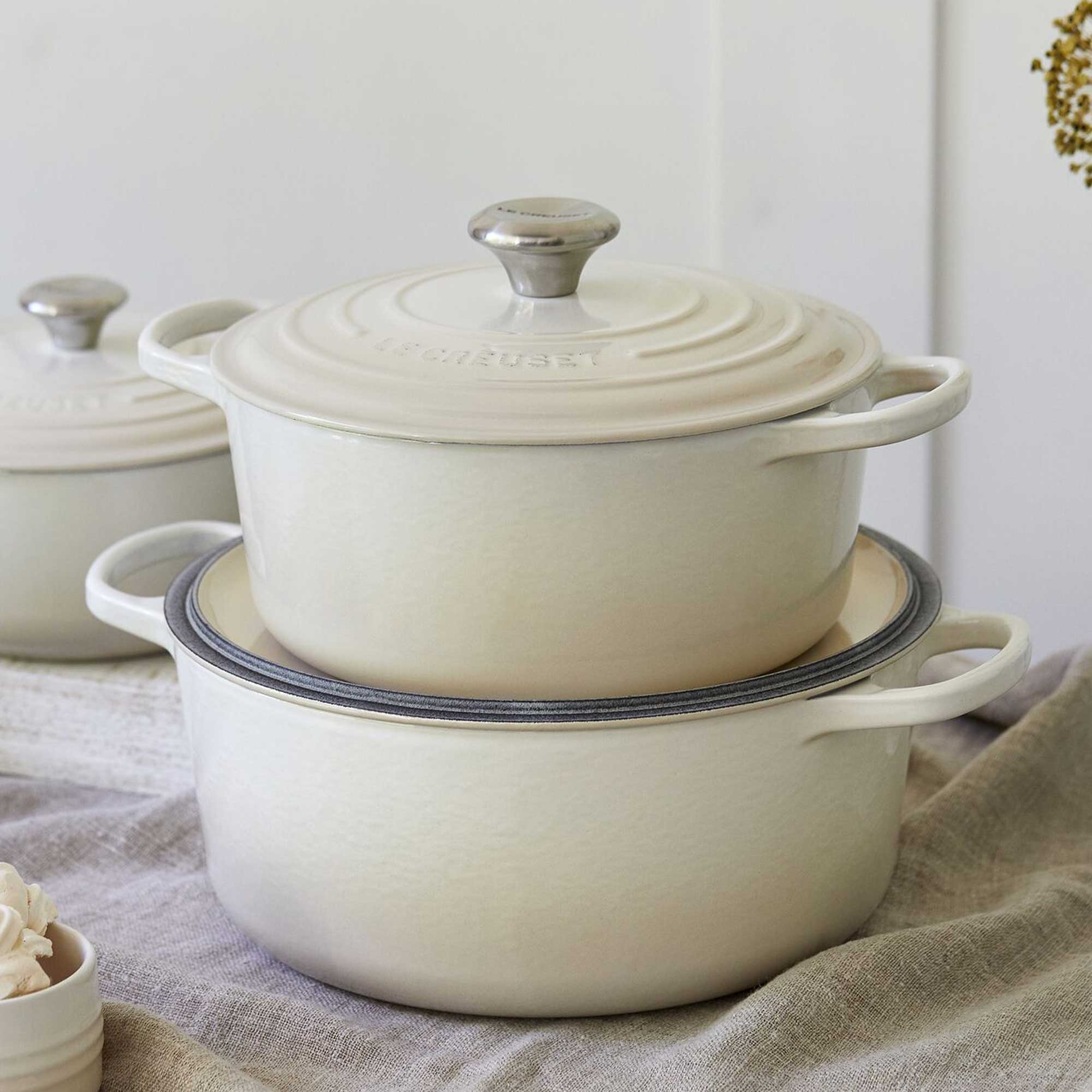 Set of cream-colored enameled cast iron cookware on a neutral background