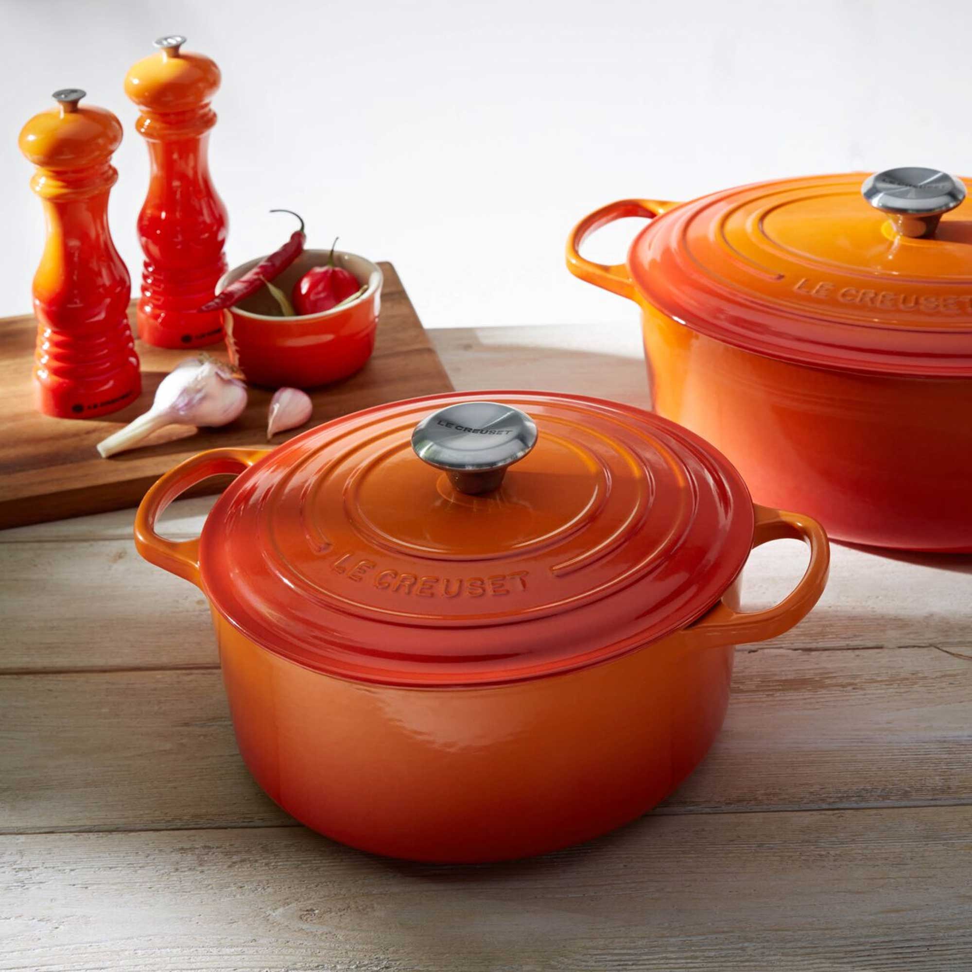 Orange Le Creuset cookware on a wooden surface with red salt and pepper shakers.