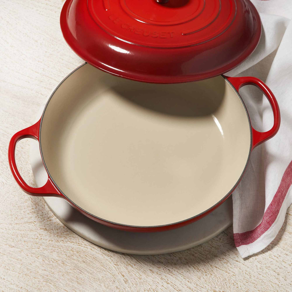 Red enameled cast iron casserole dish with beige interior on a light background