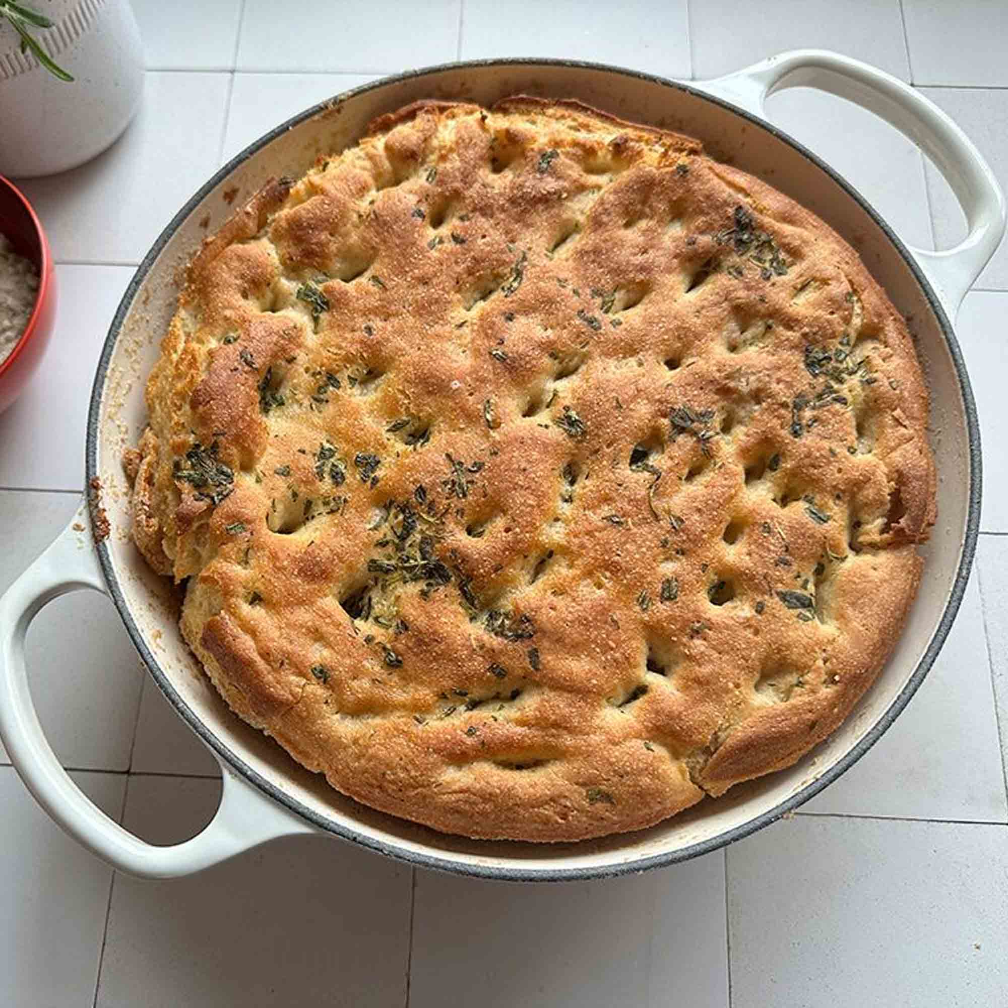 Baked bread in a round baking dish on a white tiled floor