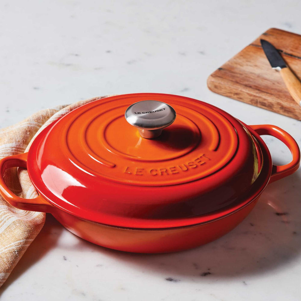 Orange Le Creuset pot on a marble surface with a wooden cutting board in the background