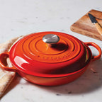 Orange Le Creuset pot on a marble surface with a wooden cutting board in the background