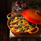 Orange casserole dish with a red lid containing a vegetable and meat dish on a wooden surface.