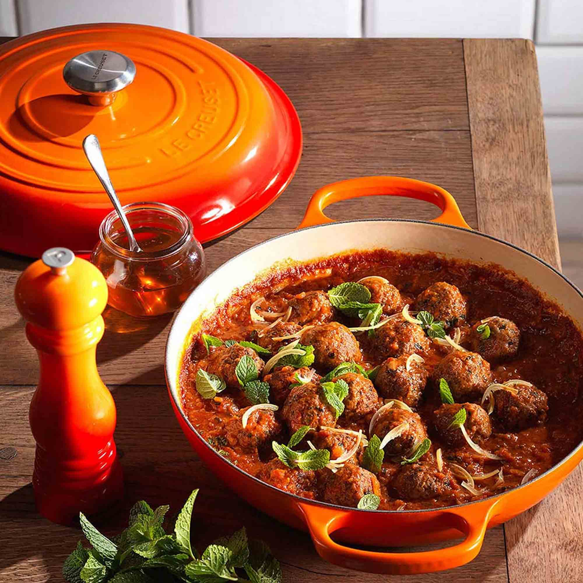 Orange Le Creuset casserole dish with meatball dish on a wooden table