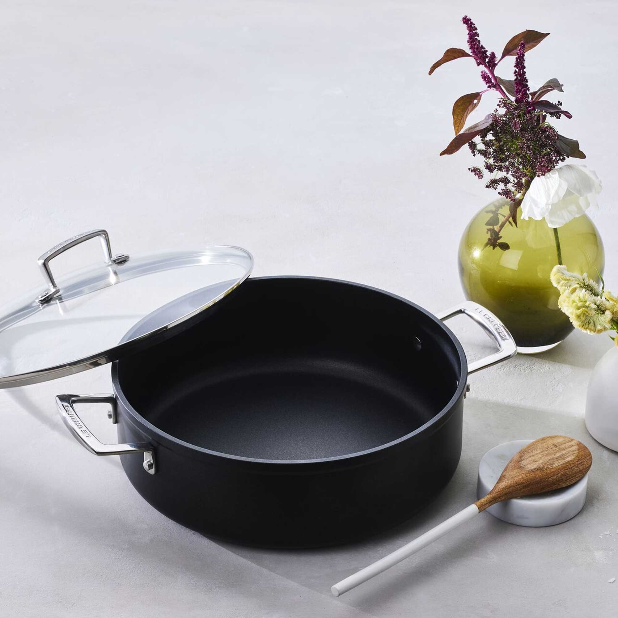 Black cookware with a wooden spoon on a light surface with decorative elements.