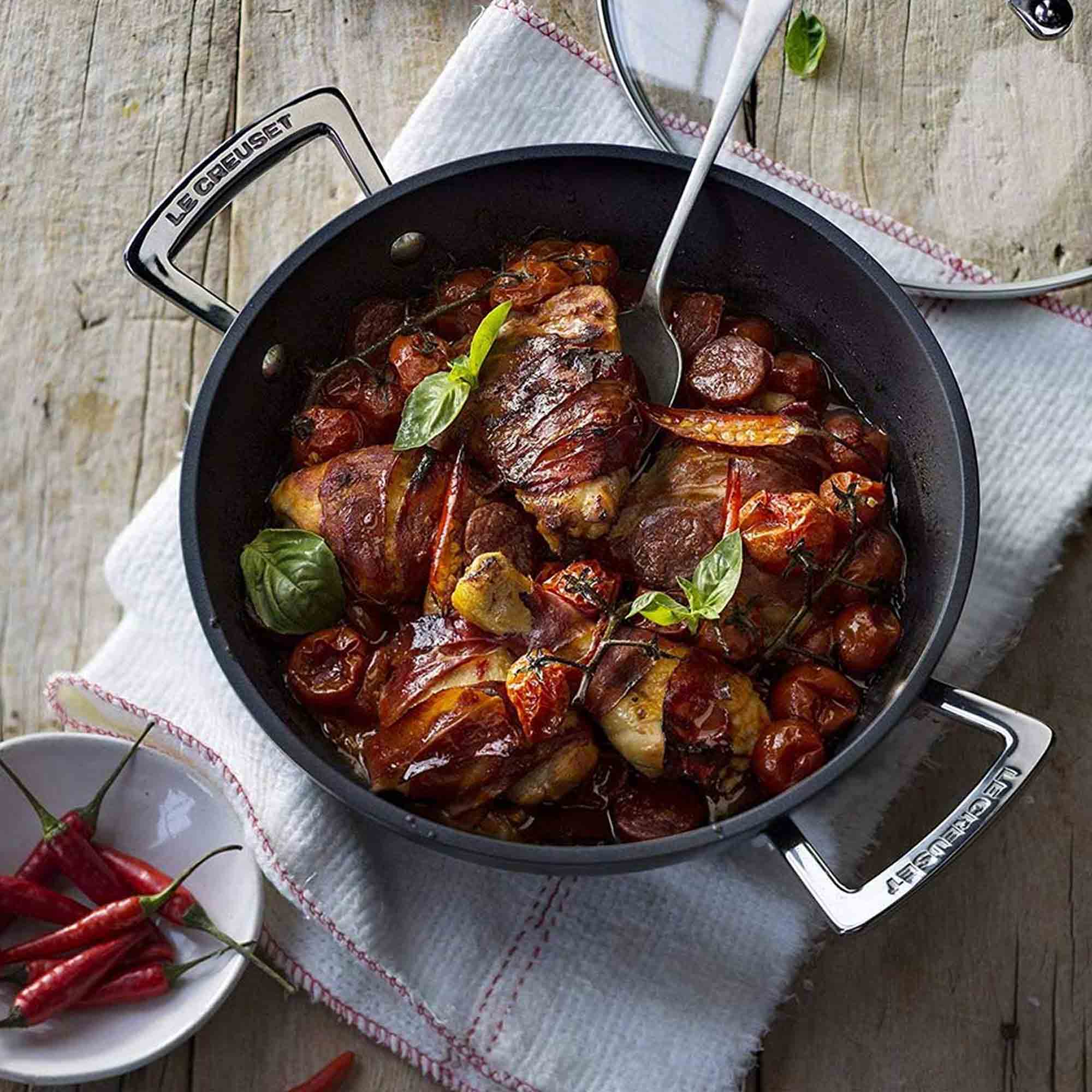 Shallow casserole with vegetables and meat in a black frying pan on a wooden surface.