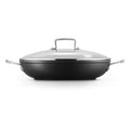Black shallow casserole with a clear glass lid on a white background