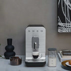 Smeg coffee machine on a countertop with a cup of coffee and ingredients.