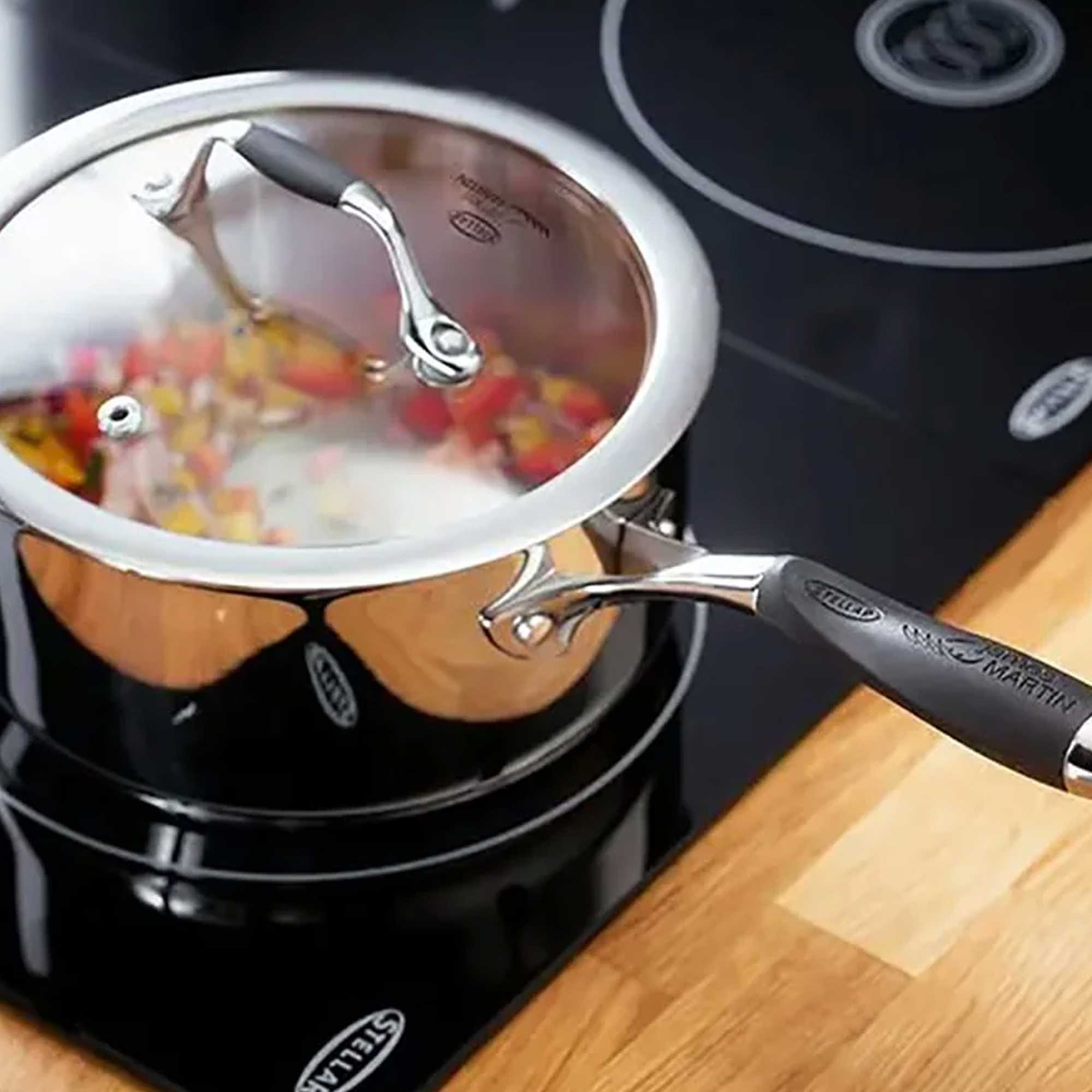 Silver saucepand with black handle on hob