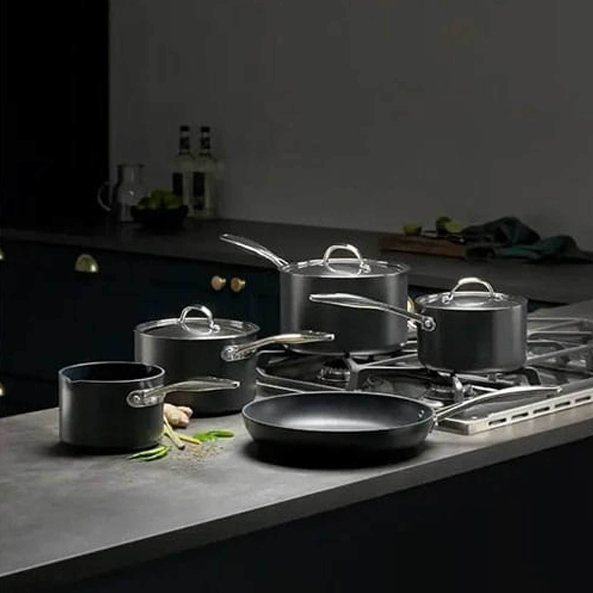 Black saucepan set with silver lids on dark grey worktop