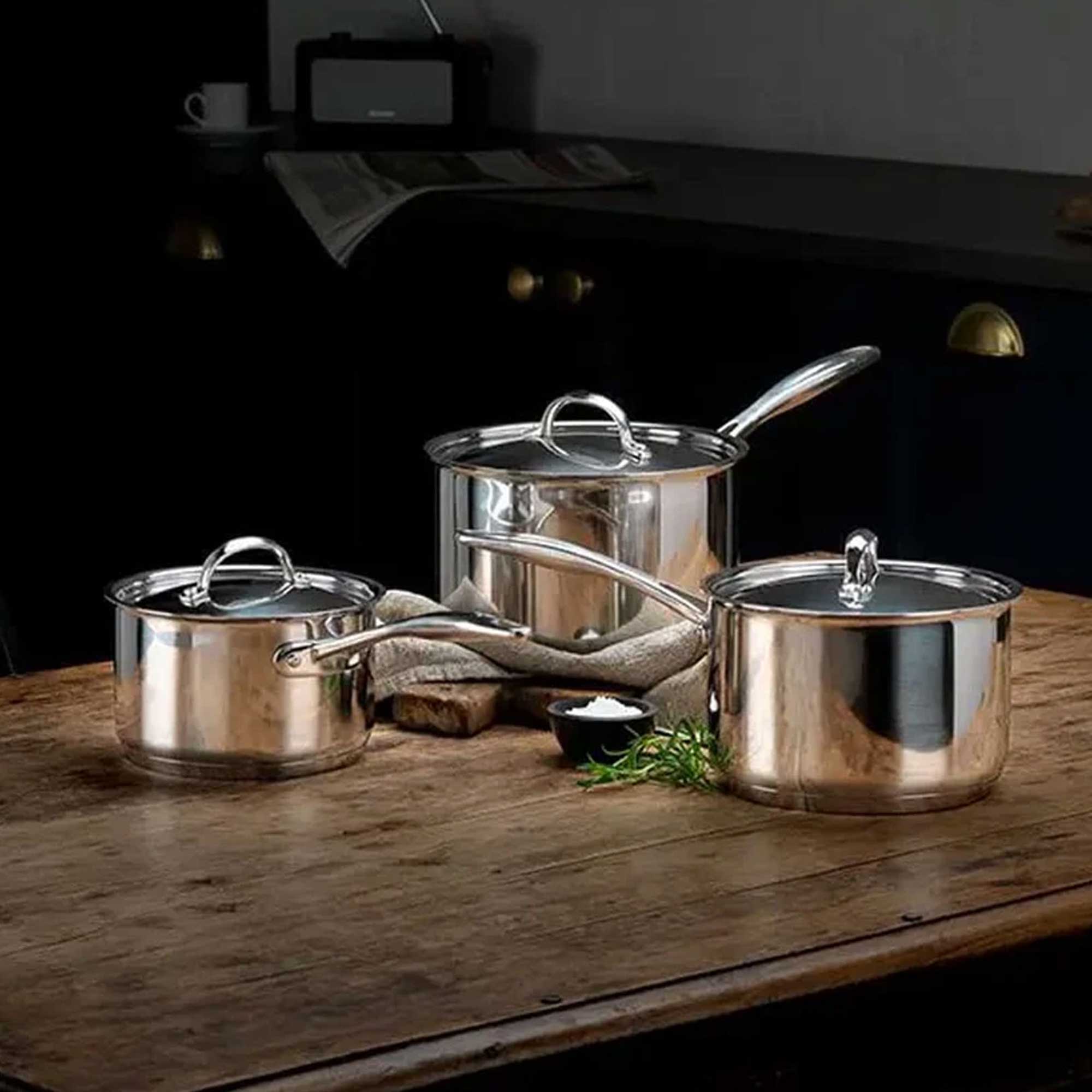 Silver saucepan set with lids on brown worktop