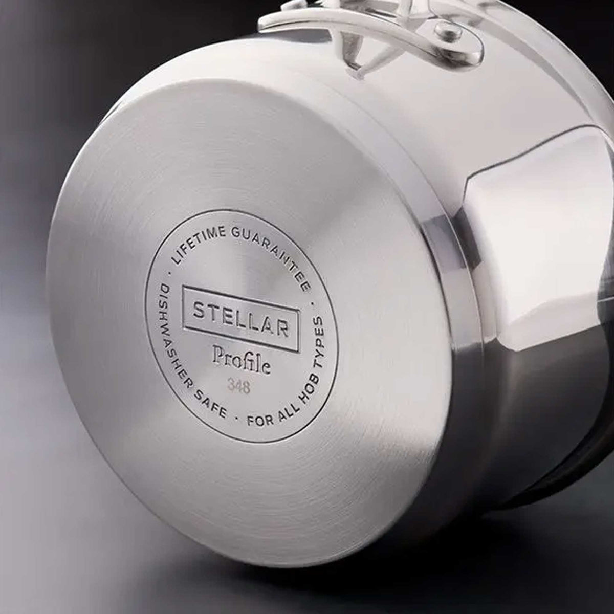 Close-up of the brushed metal base of a stainless steel pot or lid, showing engraved text that reads 'STELLAR Profile 348' and 'LIFETIME GUARANTEE' on a dark studio background.