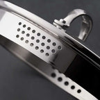 Close-up of a silver draining saucepan lid set against a dark gray background.