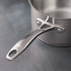 A close-up of a stainless steel saucepan handle with rivets, shown against a dark gray textured background.