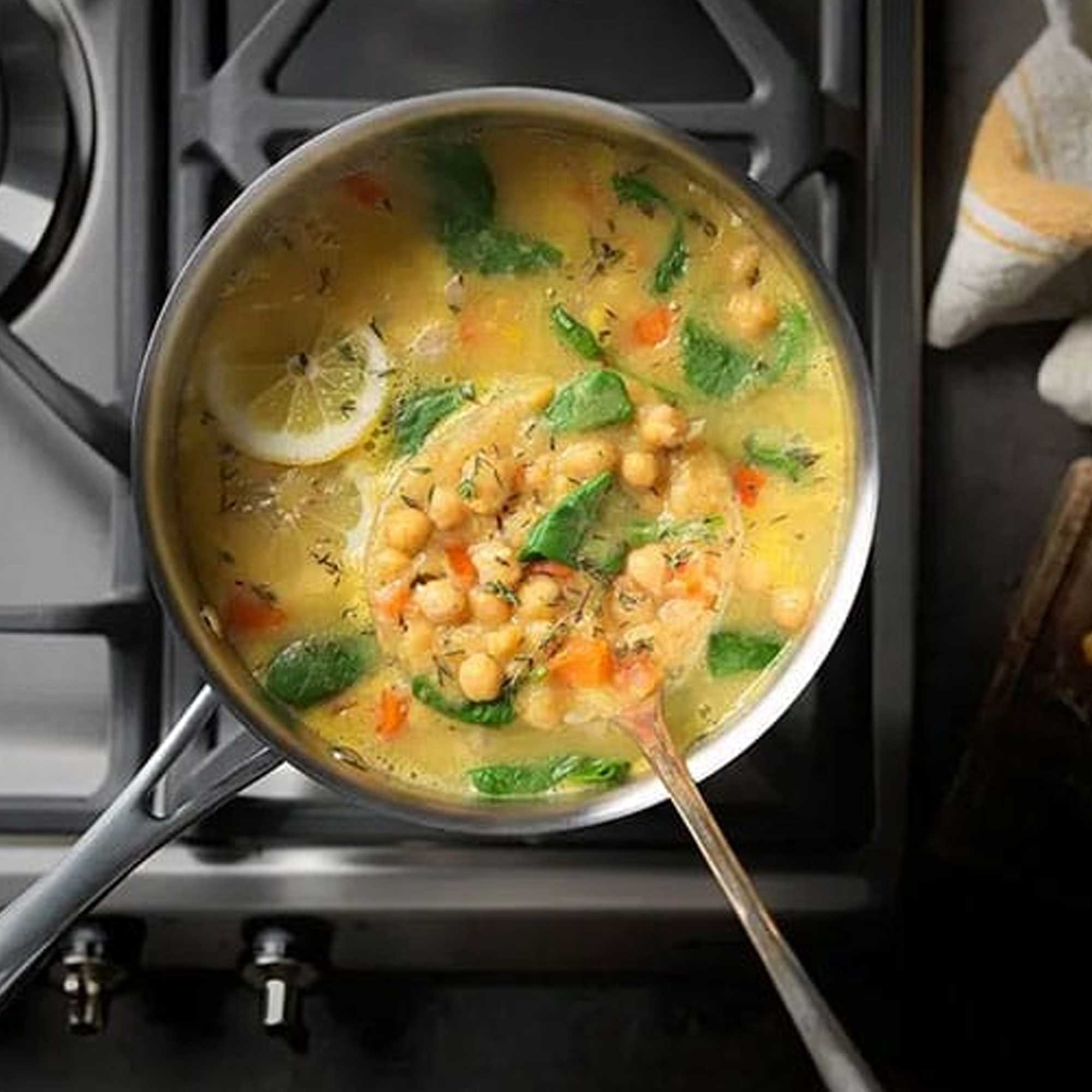 Soup with chickpeas, carrots, and spinach in a pot on a stove.