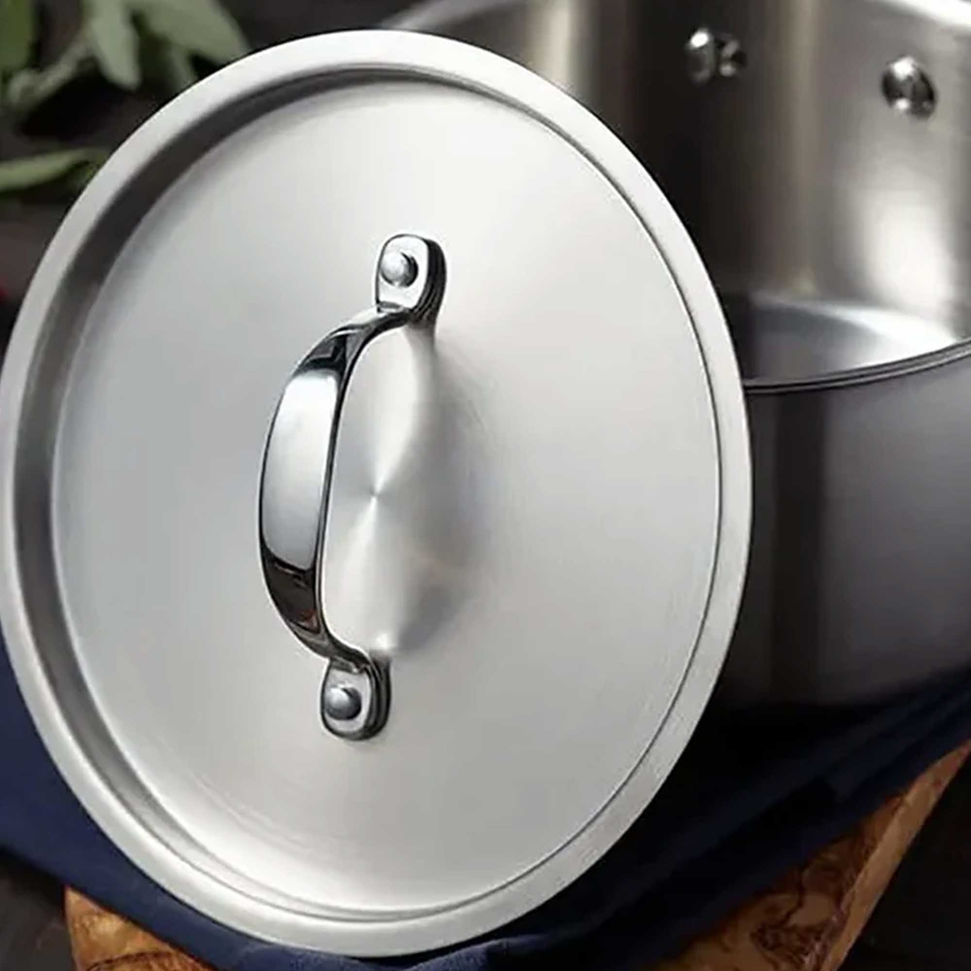 Close-up of a stainless steel pot lid with a handle on a wooden surface.