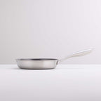 A stainless steel frying pan with a long, curved handle, shown from a side profile on a clean, light gray studio background.