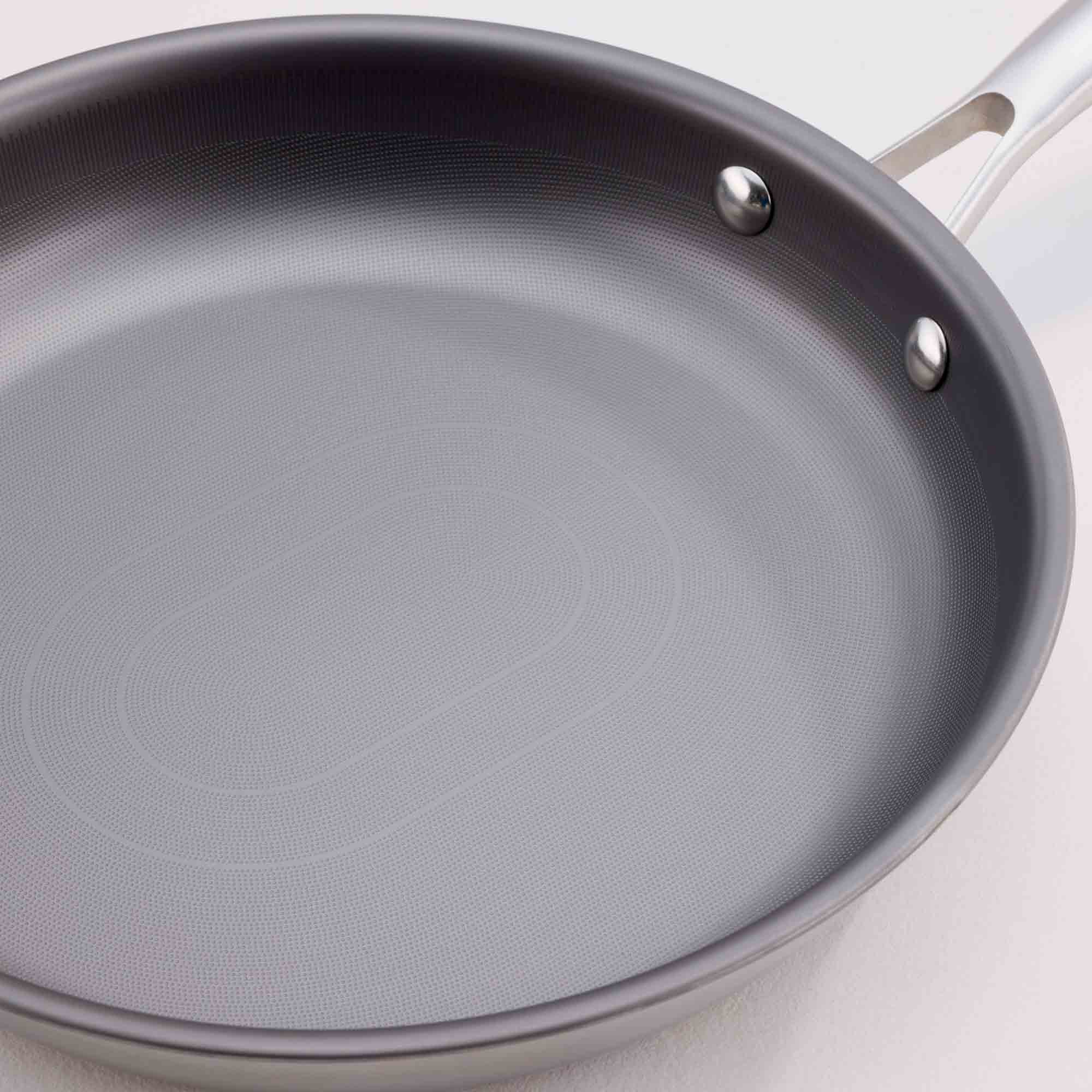 A close-up of a dark gray non-stick frying pan with a silver metal handle and rivets, set against a light off-white background.