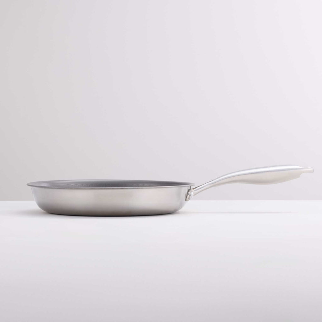 A stainless steel frying pan with a long, curved white handle, shown from a side profile on a clean white surface against a light gray background.