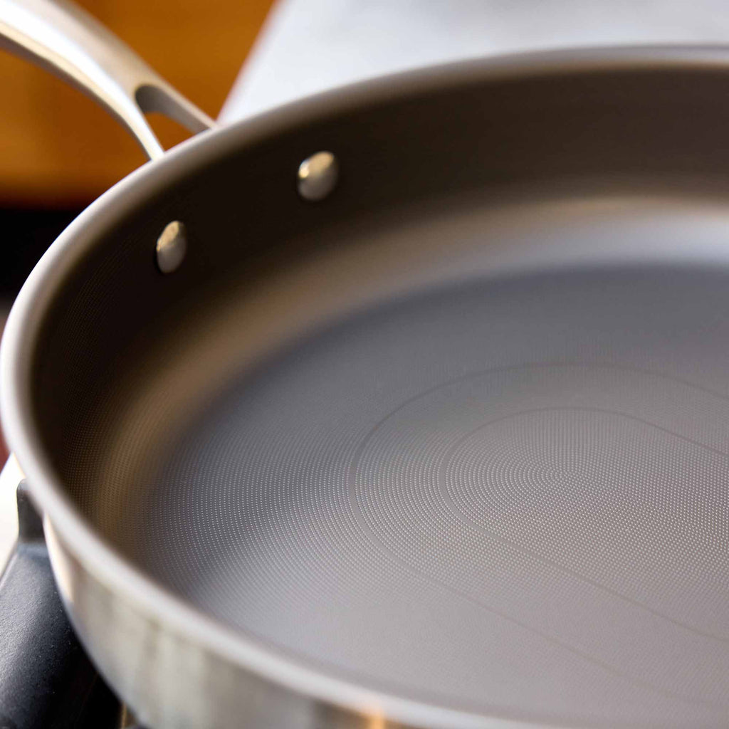 Close-up of a stainless steel saute pan with a textured non-stick interior and a metallic handle, shown on a stovetop.