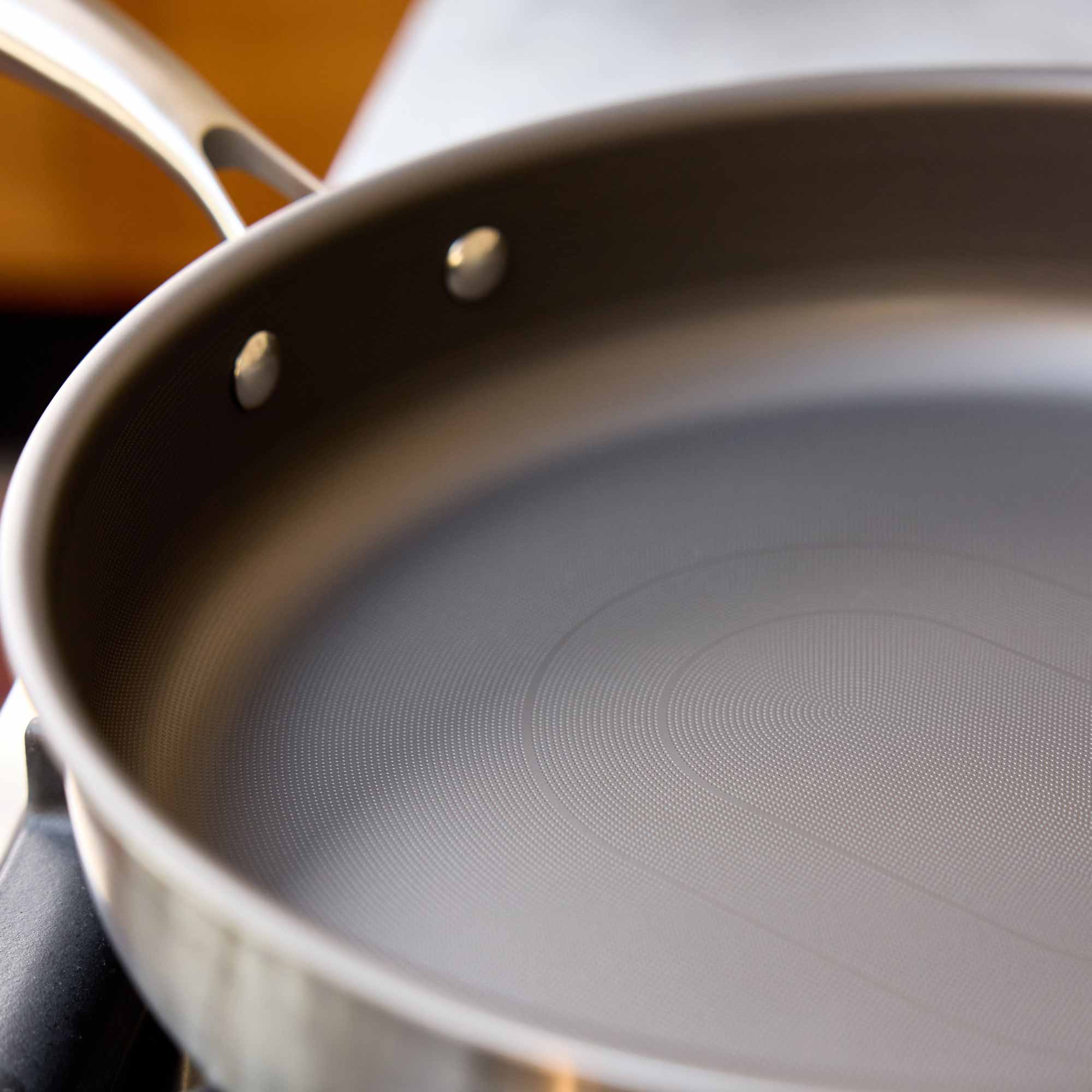 Close-up of a stainless steel saute pan with a textured non-stick interior and a metallic handle, shown on a stovetop.