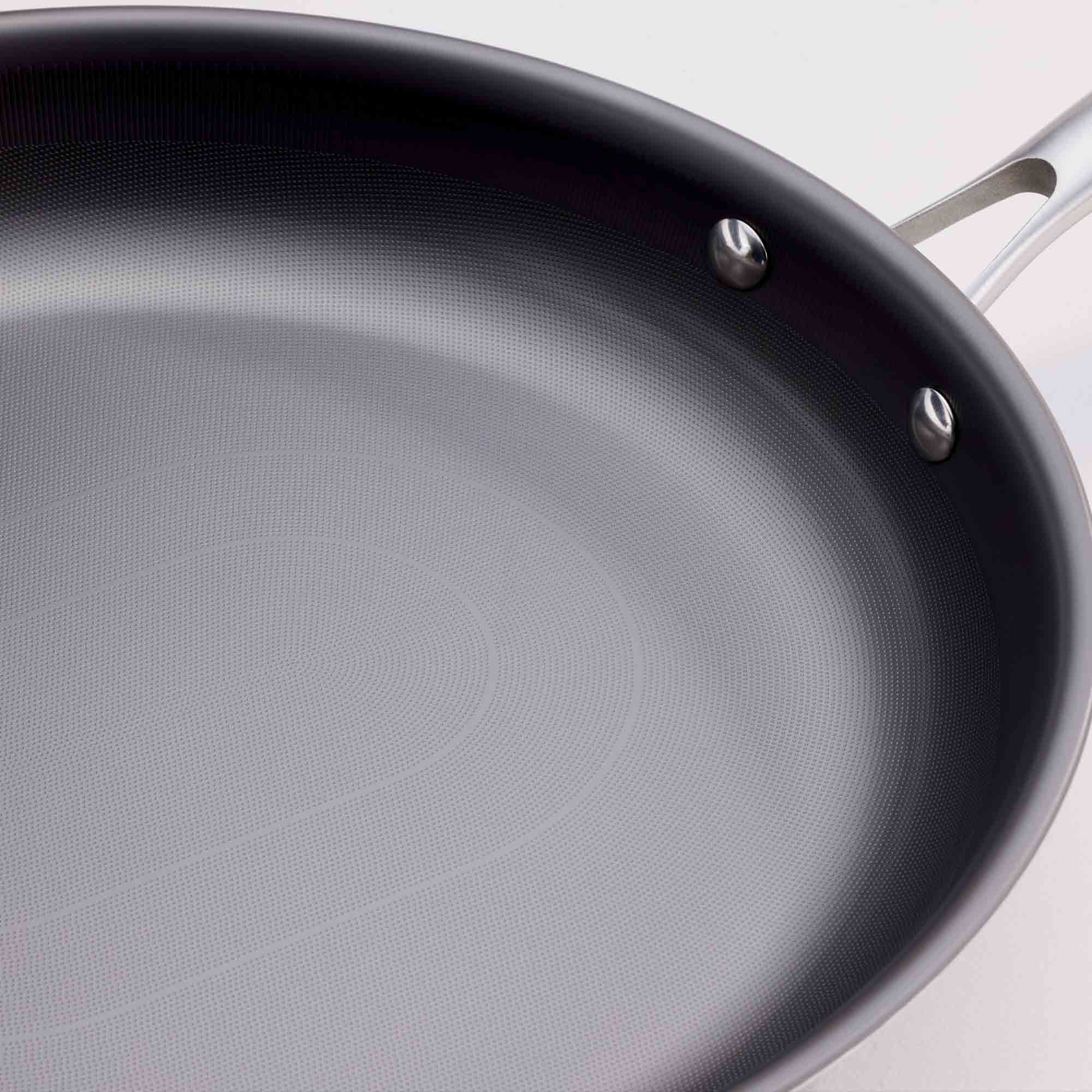 Close-up of a dark non-stick saute pan with a textured interior and a silver metal handle attachment, shown against a light background.