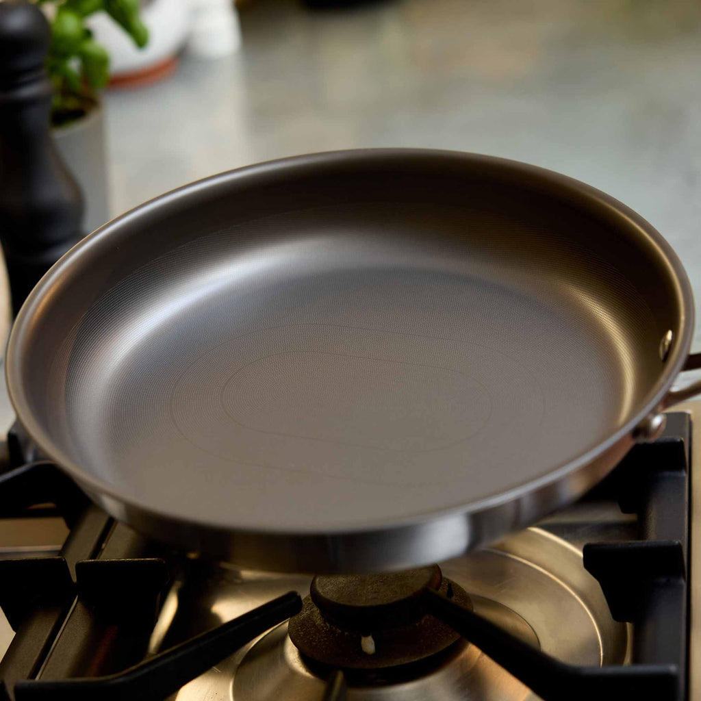 A dark non-stick frying pan sits on a gas stovetop burner in a kitchen setting.